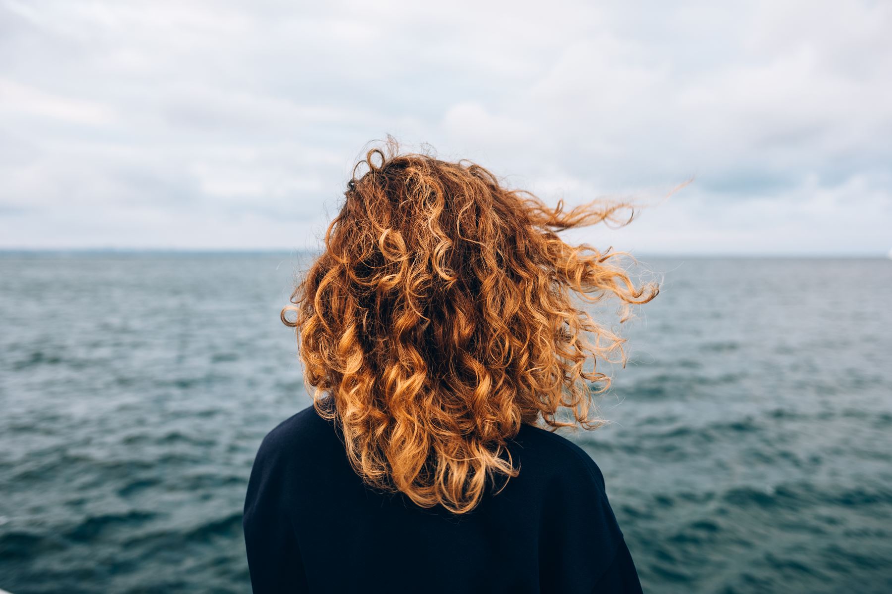Bild på en kvinna med långt brunt hår som kollar ut på havet
