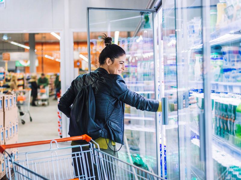 Bild på en kvinna som tar en produkt ut ur kyldisken i en matbutik