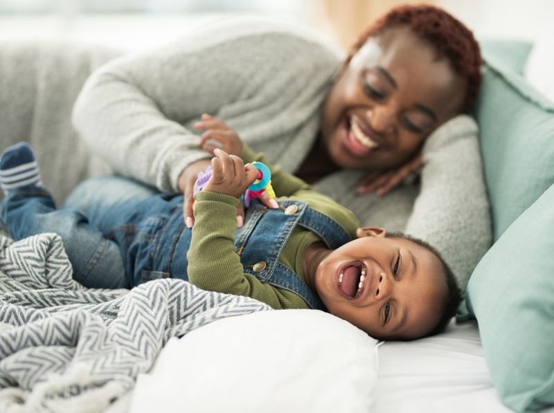 En kvinna busar med bebis i en soffa och båda skrattar