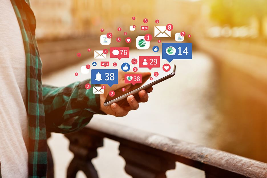 närbild på hand som håller i en mobiltelefon och runt telefonen syns massa emojis och symboler som representerar engagemang på sociala medier