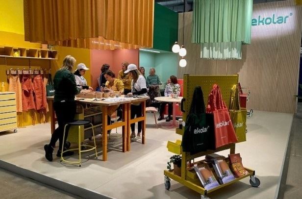 Färgstark monter för Lekolar med många besökare där några står och pysslar vid ett ståbord