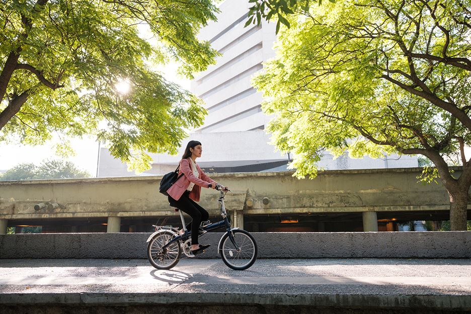 Kvinna på cykel med träd och byggnad i bakgrunden