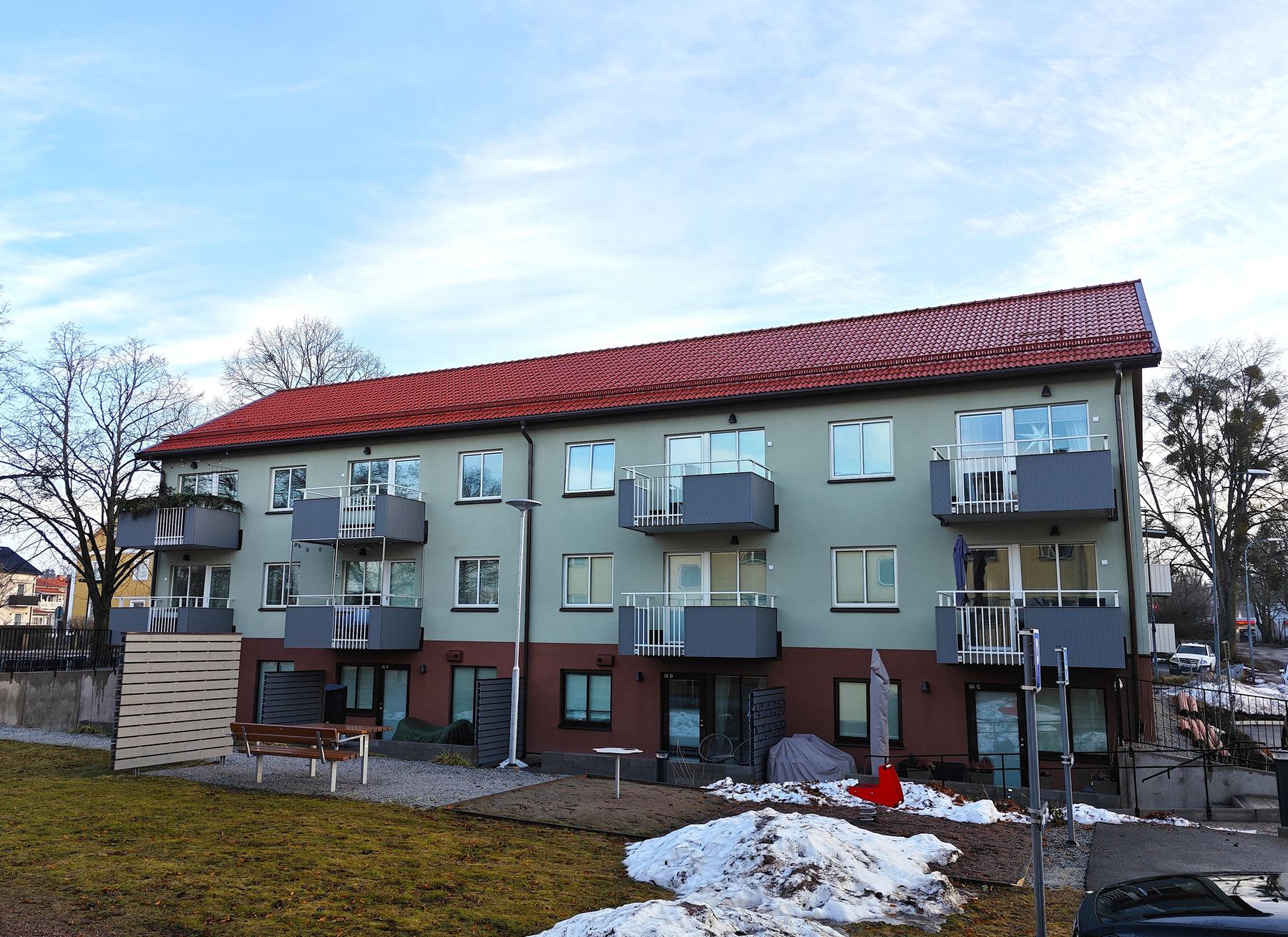 Flerbostadshus Bostjärnan i tre våningar med balkonger. Sällskapsyta i förgrunden med bänk, bord, bollplank och liten lekplats.