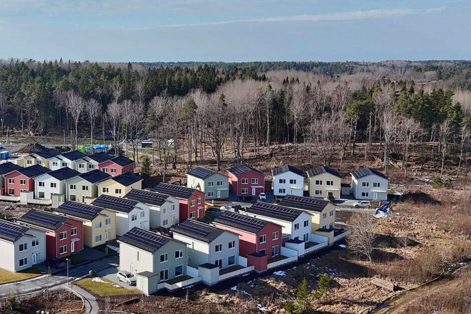 Färgglada småhus med solpaneler på taket på en öppen ängsyta med träd i bakgrunden. Småhusen är Fjärilshusen från Bonava i Järfälla.