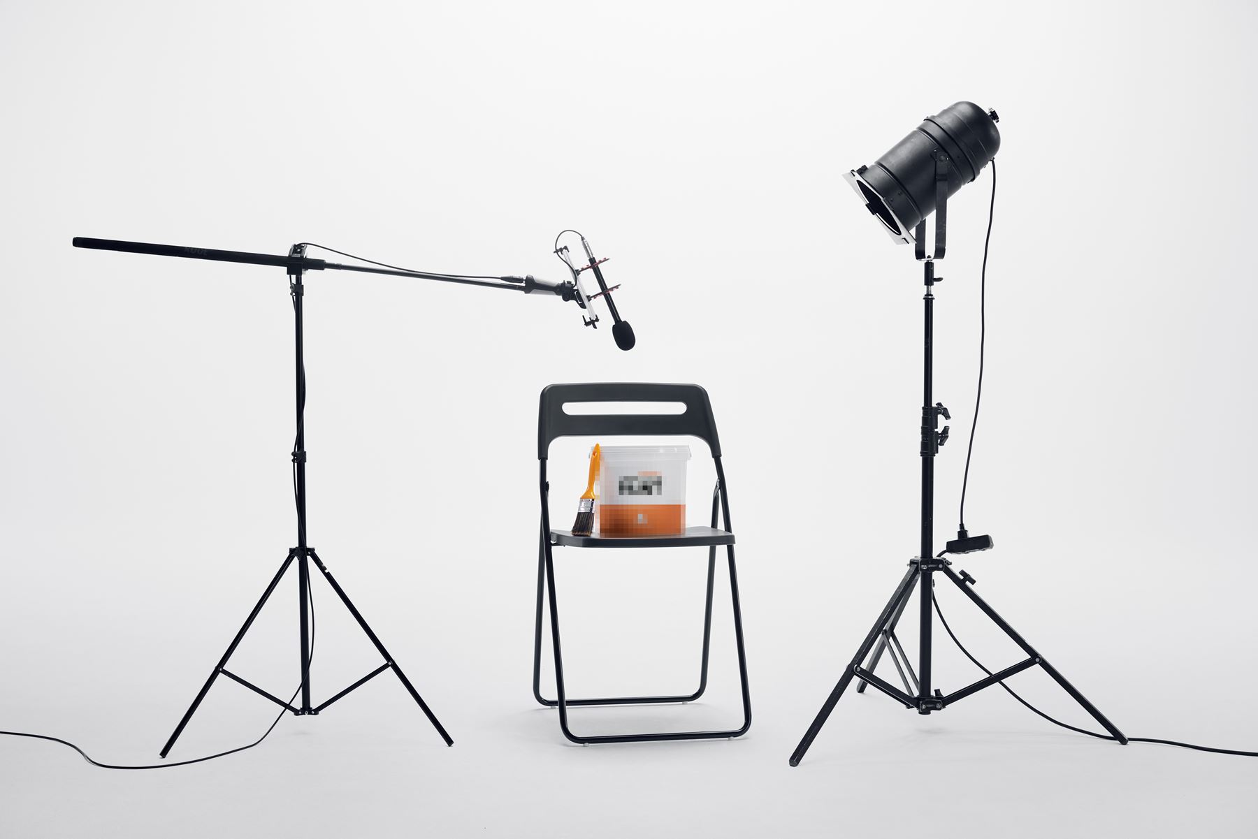 En suddad anonym målarfärgburk står på en stol med en mikrofon och lampa riktad mot sig. 