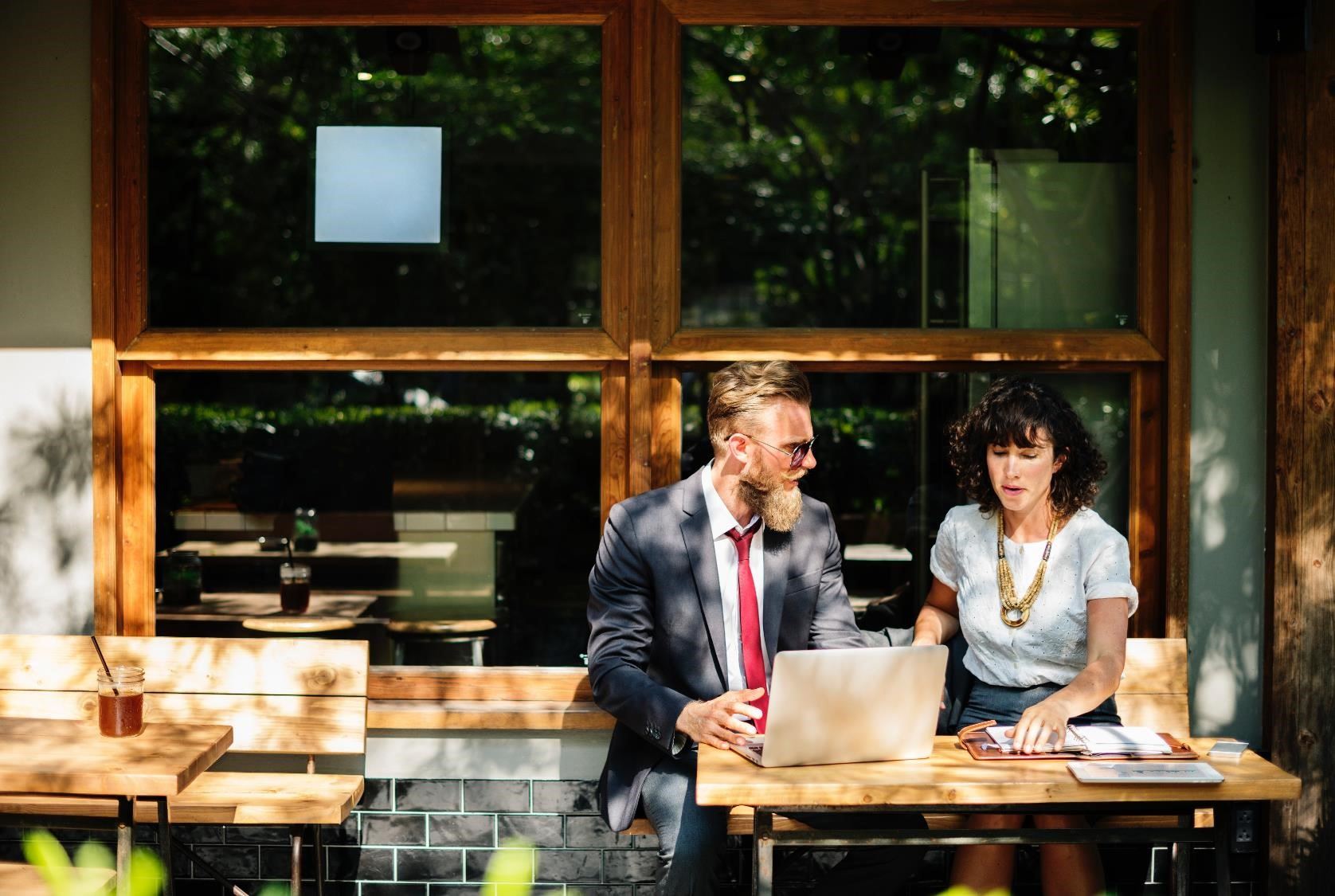 A man and a woman outside a cafe, looking at a computer and a notebook