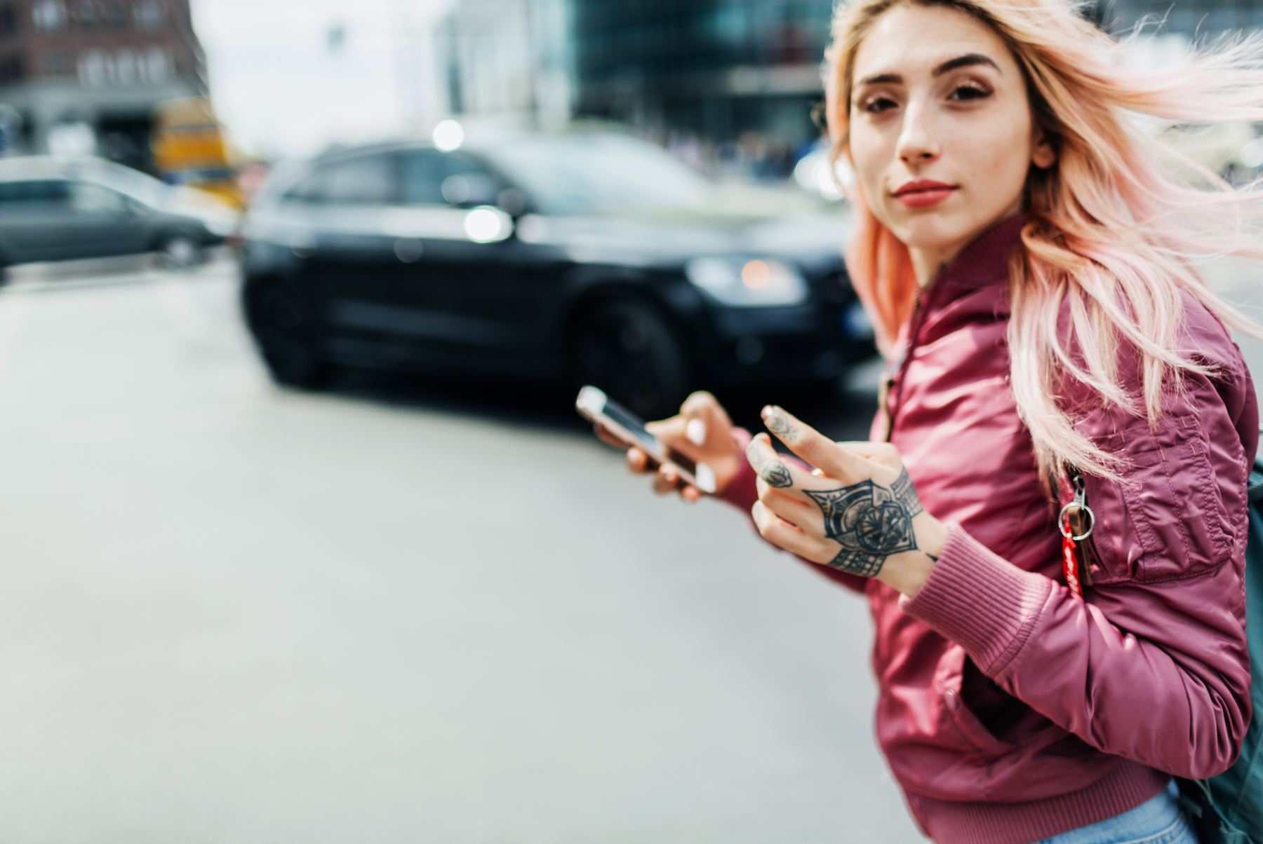 Ung cool kvinna tittar upp från sin mobil på väg över gatan