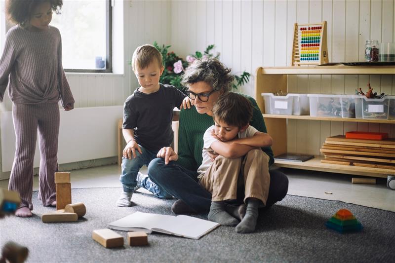 Tre barn och en vuxen sitter på en grå matta och läser en bok